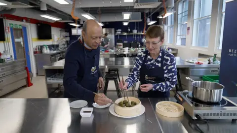 Kevin Church/BBC News Pallab Ghosh and Helen Sharman picking up green coloured dumplings with chopsticks.