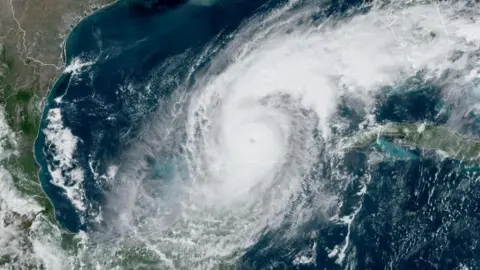 Noaa/Reuters Satellite image of Hurricane Milton over the Gulf of Mexico. There are swirling clouds around the eye of the hurricane, with blue ocean underneath. The coastlines of south-east USA and east Mexico are visible on the west (left) of the image.